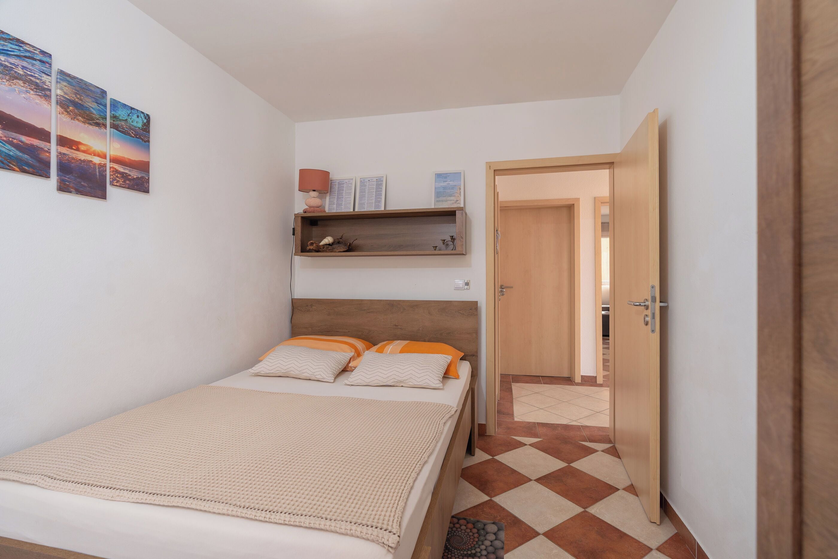 Une chambre à coucher comprenant un lit, une tête de lit en bois, une étagère avec des objets décoratifs et une porte donnant sur une autre pièce.