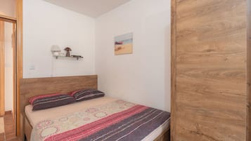 A bedroom with a wooden headboard, a bed with patterned bedding, a small shelf with decorative items, and a beach-themed wall art.