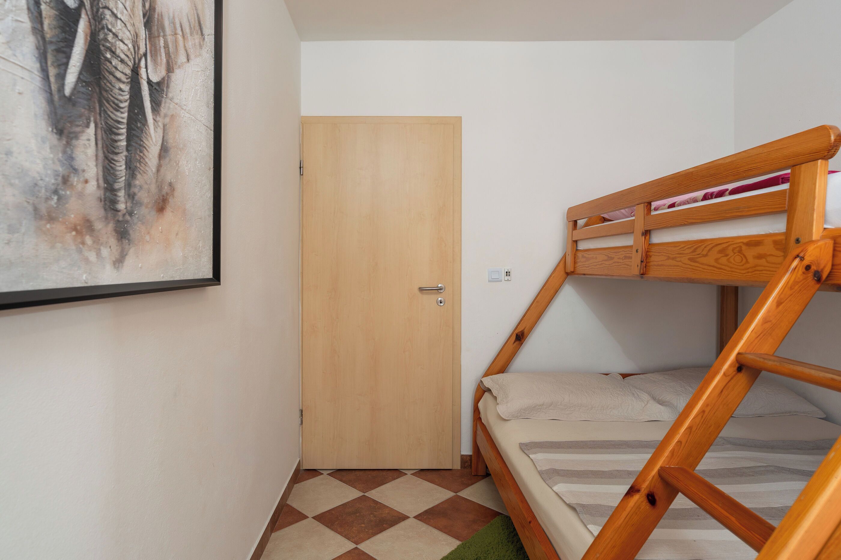 Una stanza piccola con un letto a castello, una porta di legno e un quadro appeso al muro.