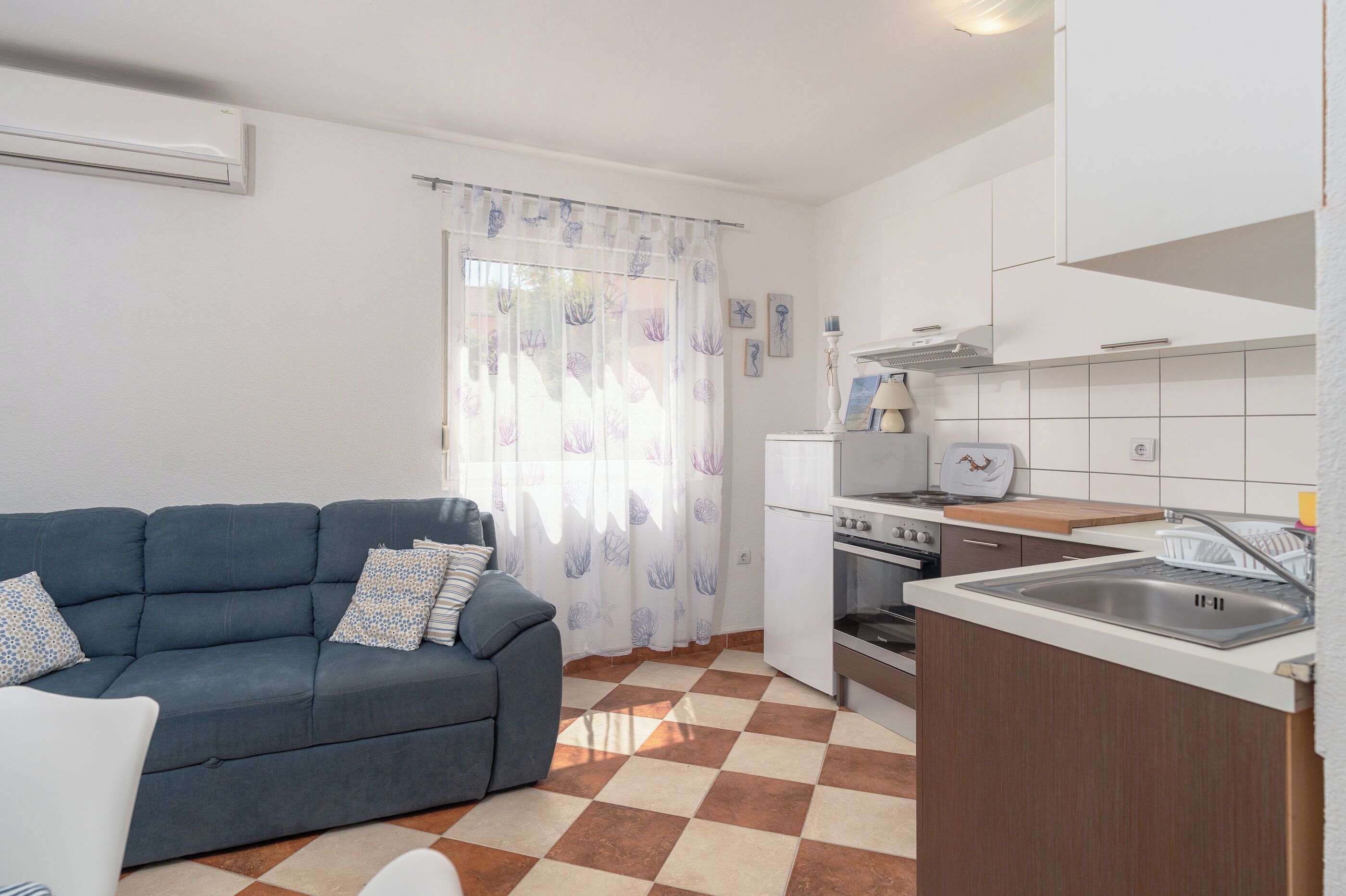 Un espacio habitable compacto con kitchenette, un sofá con cojines estampados y un suelo a cuadros.