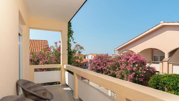 Ein Balkon mit Blick auf benachbarte Häuser, einem Stuhl und blühenden, rosa Pflanzen.