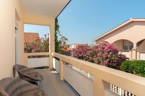Un balcon donnant sur les maisons voisines, une chaise et des plantes à fleurs roses.