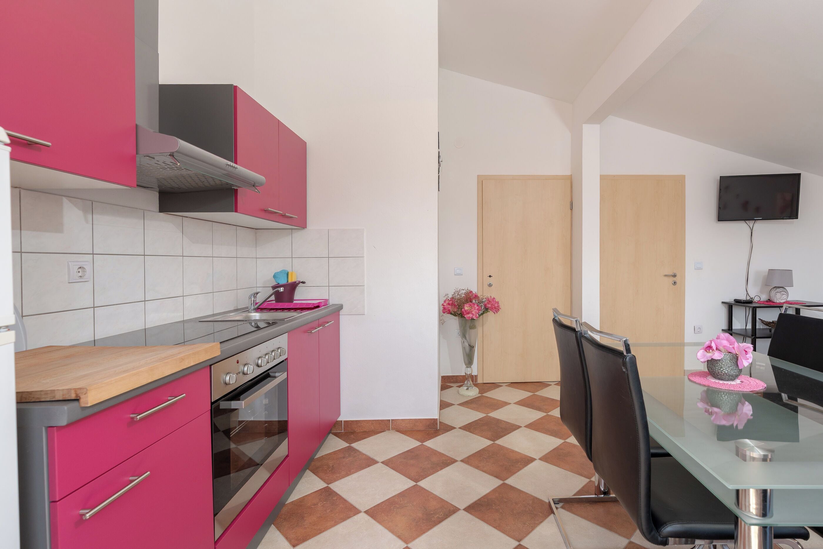 A modern kitchen with pink cabinets, a stainless steel oven, and a dining area with a glass table and black chairs.