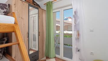 A bedroom with a bunk bed, a wardrobe, a sliding glass door leading to an outdoor area, and a green curtain.