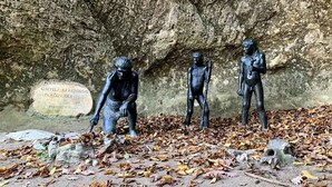 Drei Bronzestatuen auf einer Steinoberfläche, im Hintergrund eine Höhle und eine Gedenktafel.