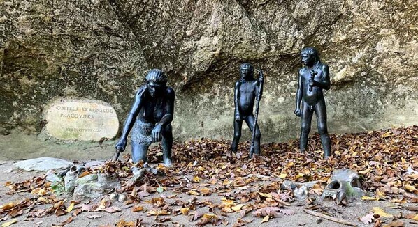 Three bronze statues on a stone surface with a cave-like background and a plaque. - Apartment Vanja (Krapina)