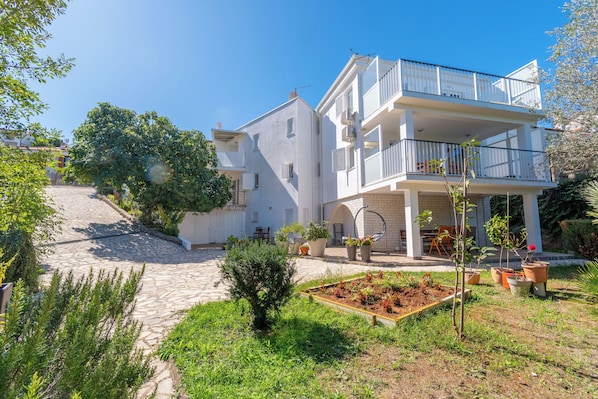 A two-story building with a balcony, a stone pathway, and a garden area. - Apartments Vlado (Omisalj)