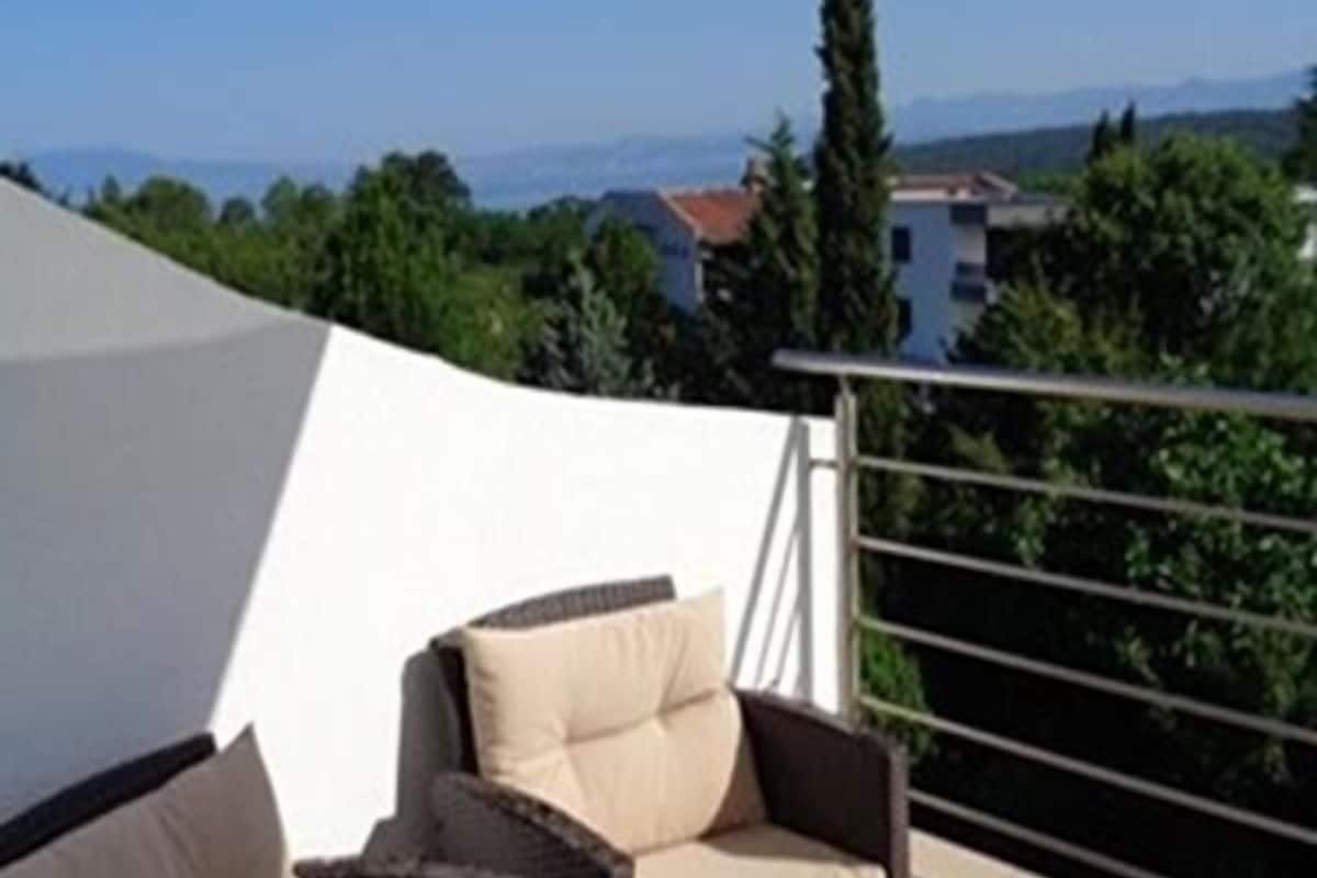 Un balcone esterno con mobili in vimini e una tenda bianca.