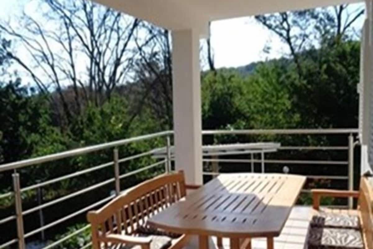 Veranda coperta con tavolo e panche in legno, circondata da una ringhiera in metallo.