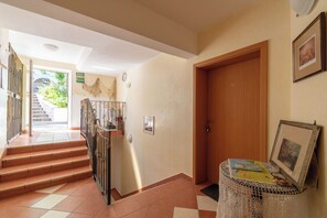 Un couloir avec un escalier menant à un espace extérieur, une porte en bois et une petite table sur laquelle se trouvent une carte et un tableau encadré.