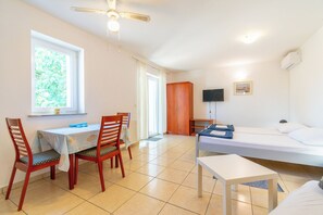 Una habitación con cama, escritorio y sillas, televisor y ventana con cortinas.