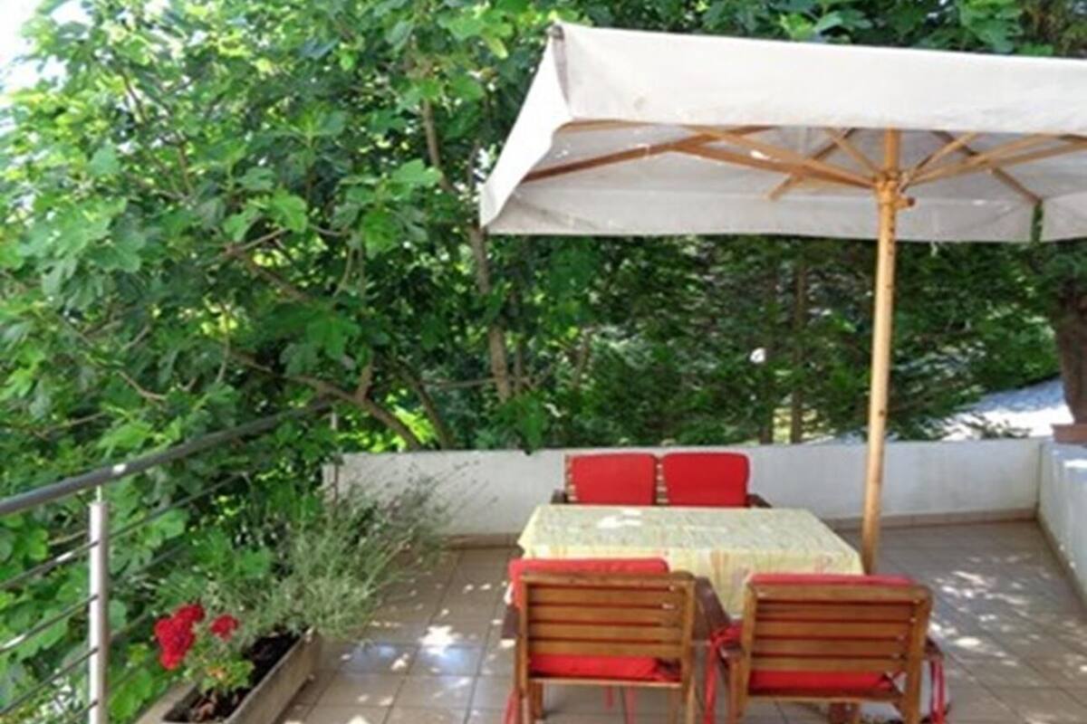 Una veranda con tavolo e sedie, riparata da un tetto e circondata dal verde.