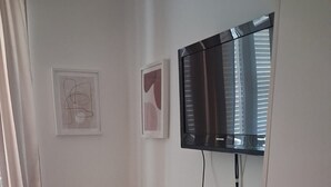 Una stanza con una scrivania bianca, una poltrona gialla, una TV a schermo piatto montata a parete e due quadri appesi.