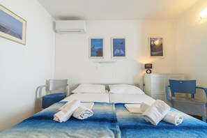 Une chambre d’hôtel avec deux lits, un bureau, une chaise et des œuvres d’art accrochées aux murs.
