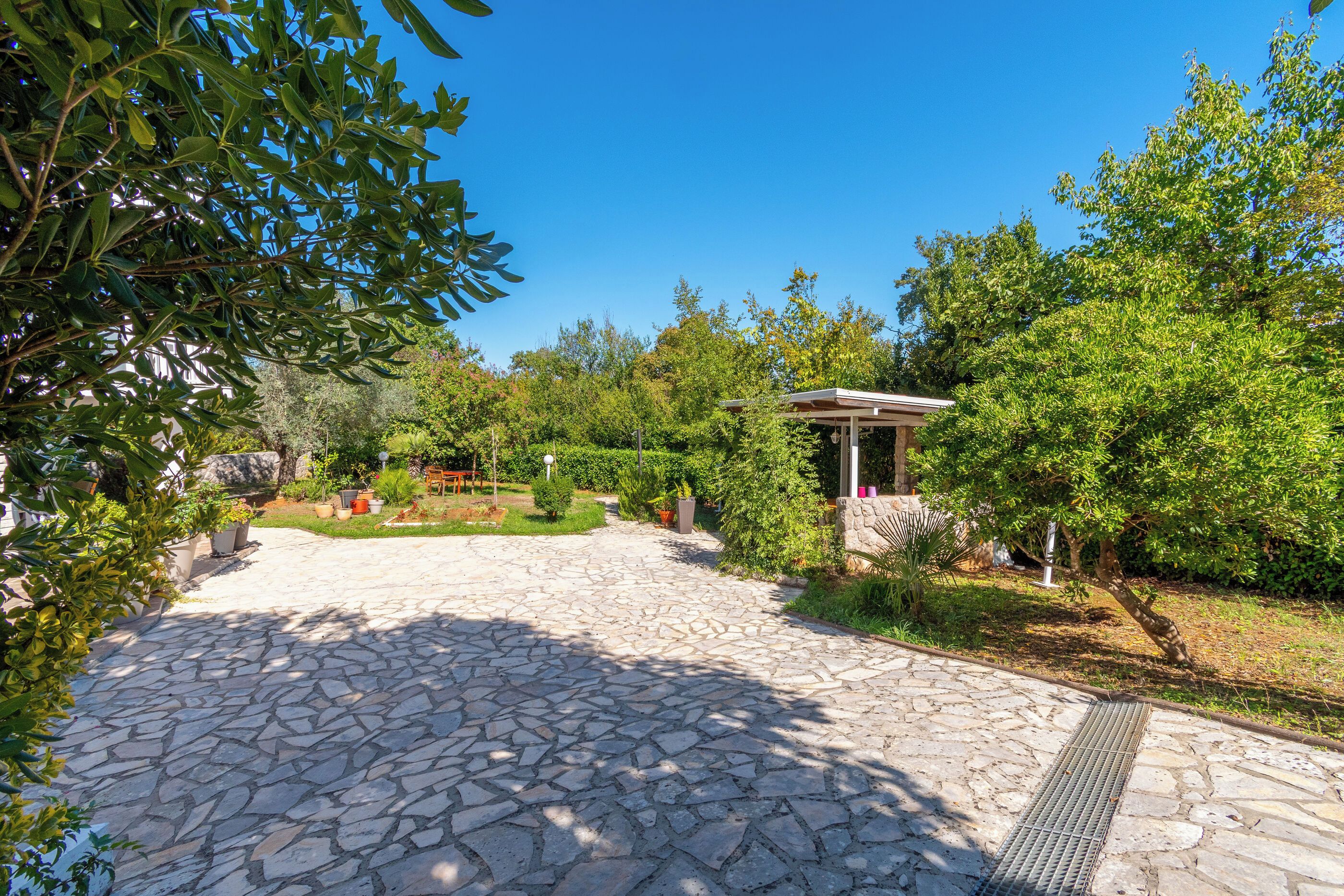 A stone-paved pathway leading to a small pavilion surrounded by lush greenery and trees.