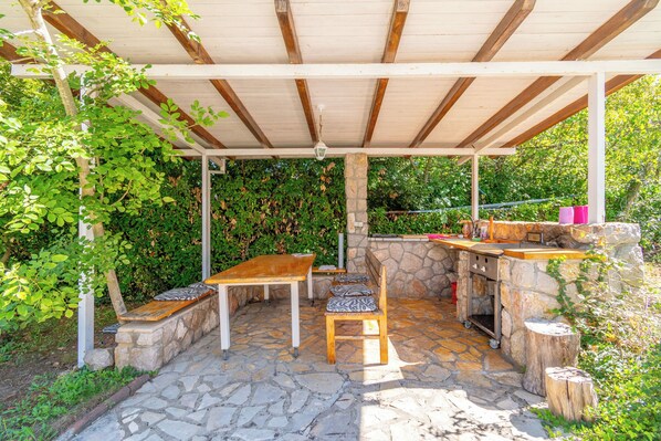 Une terrasse extérieure dotée d’un sol en pierre, d’une table et de chaises en bois, d’un mur en pierre et d’une pergola au-dessus.