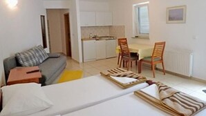 Un ambiente compatto con divano, un piccolo tavolo, un'area pranzo con sedie e un angolo cottura.