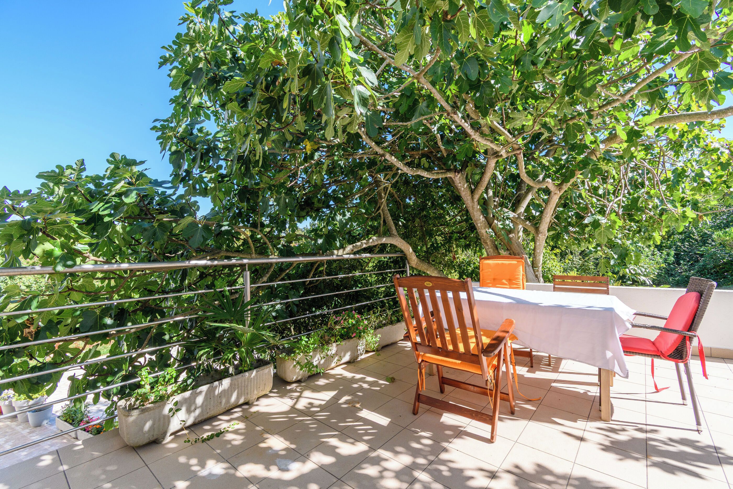 An outdoor patio with a table and chairs, surrounded by a metal railing and a tree.