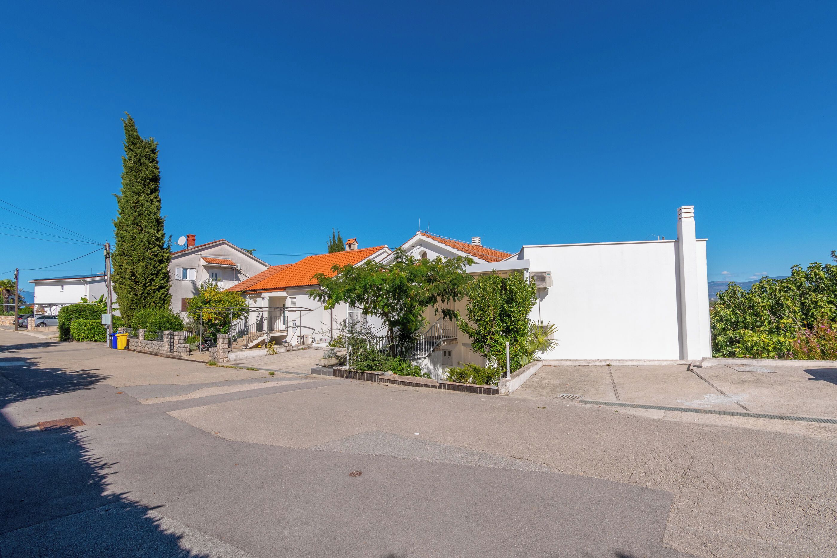 A residential street with houses, a clear sky, and a distant view of the sea.