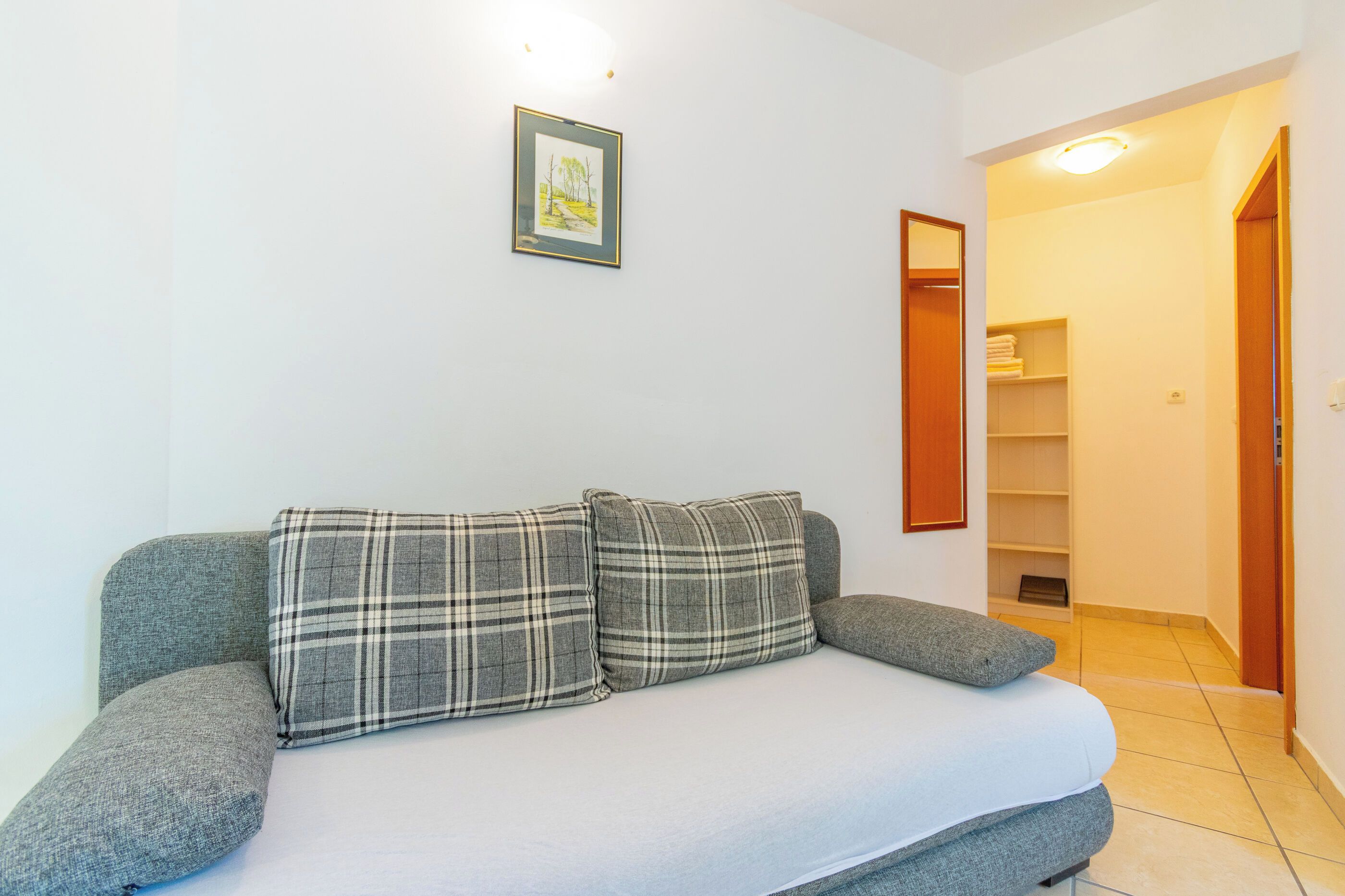 Ein Zimmer mit einem grauen Sofa, einem gerahmten Bild an der Wand und einer Holztür zu einem Flur.