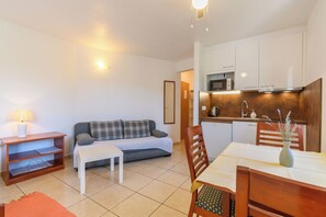 Un espacio habitable compacto con kitchenette, un sofá, una mesa de comedor y una lámpara.