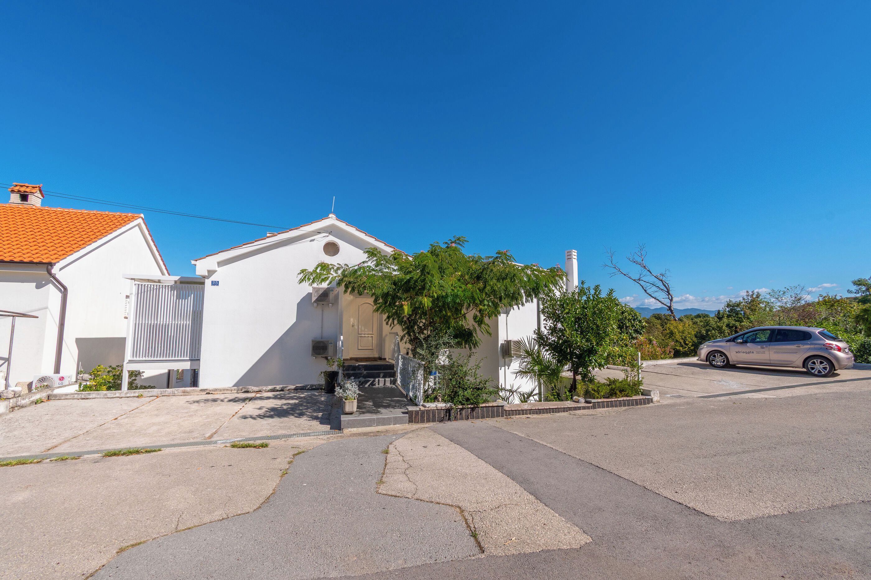 A residential street with a white house, a car parked on the side, and a clear blue sky.