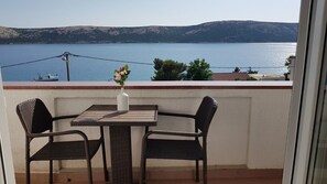 Ein Balkon mit Korbstühlen und einem Tisch, der auf ein Gewässer und Hügel blickt.
