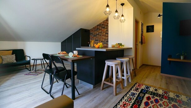 A modern kitchen with a brick backsplash, a dining area with a wooden table and chairs, and a colorful rug. - Apartments Secret Garden (Razanac)