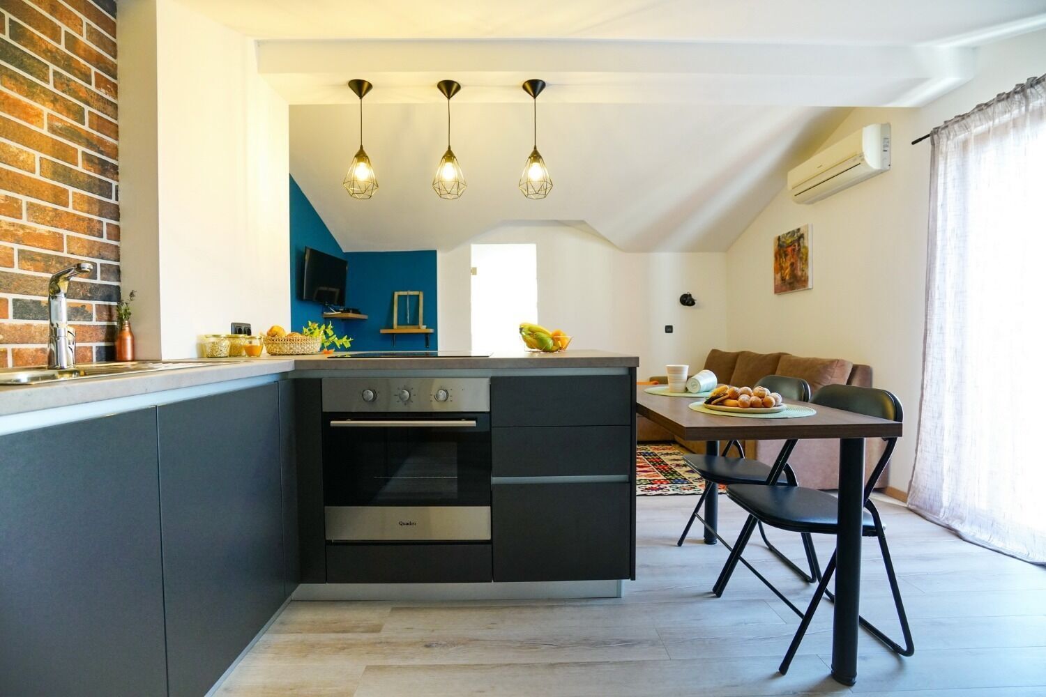 Una cocina moderna con horno integrado, un comedor con mesa y sillas, y una sala de estar con sofá y televisor.