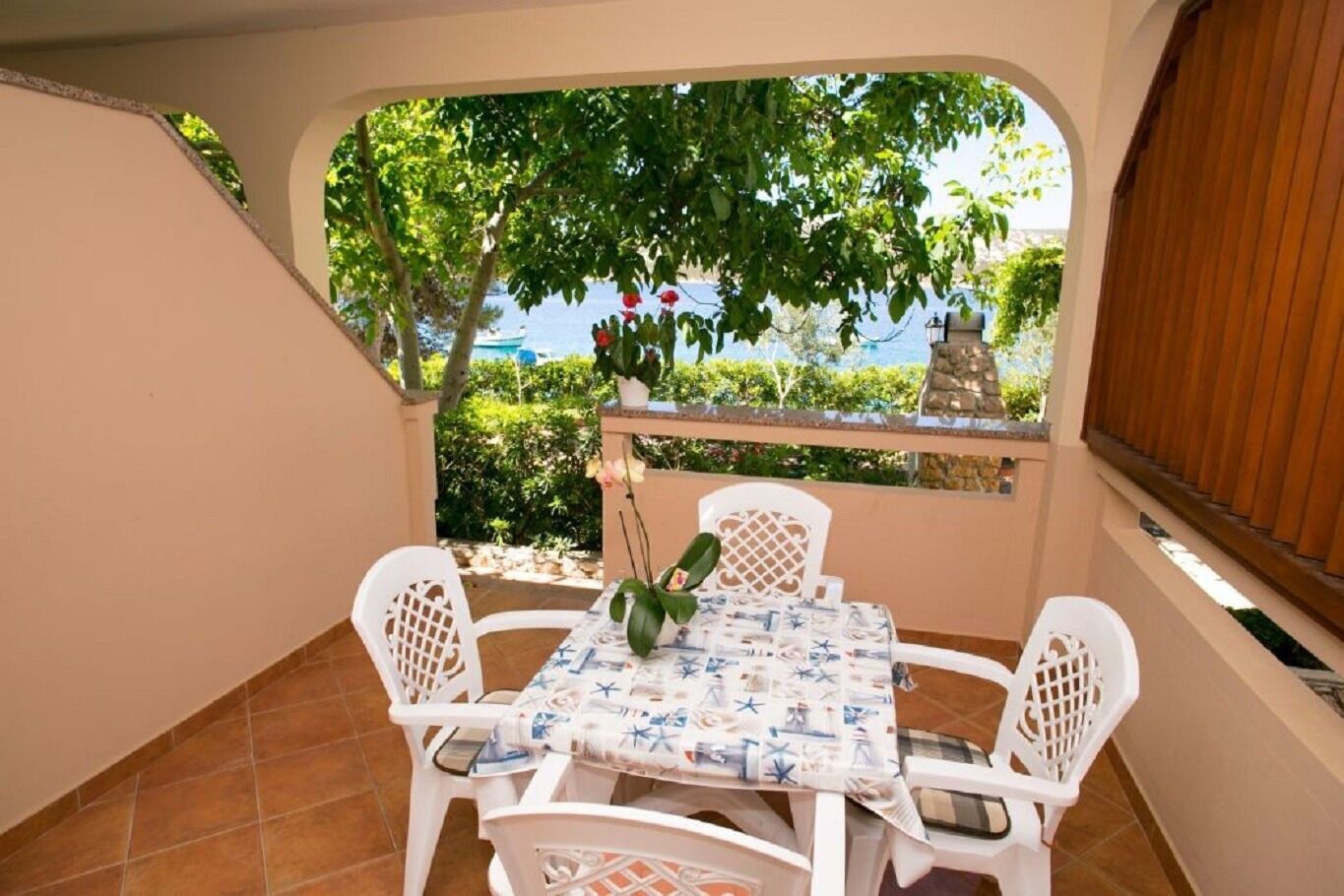 A small outdoor patio with a table and four chairs, surrounded by a low wall and a view of the sea.