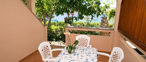 A small outdoor patio with a table and four chairs, surrounded by a low wall and a view of the sea.