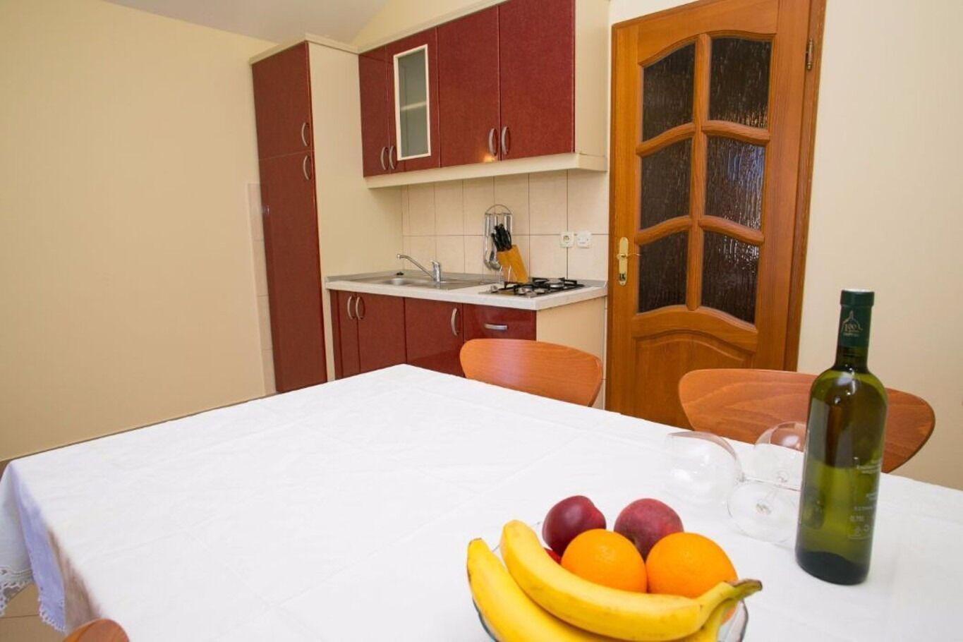 A small kitchen with a table set for dining, a fruit bowl, and a bottle of wine.