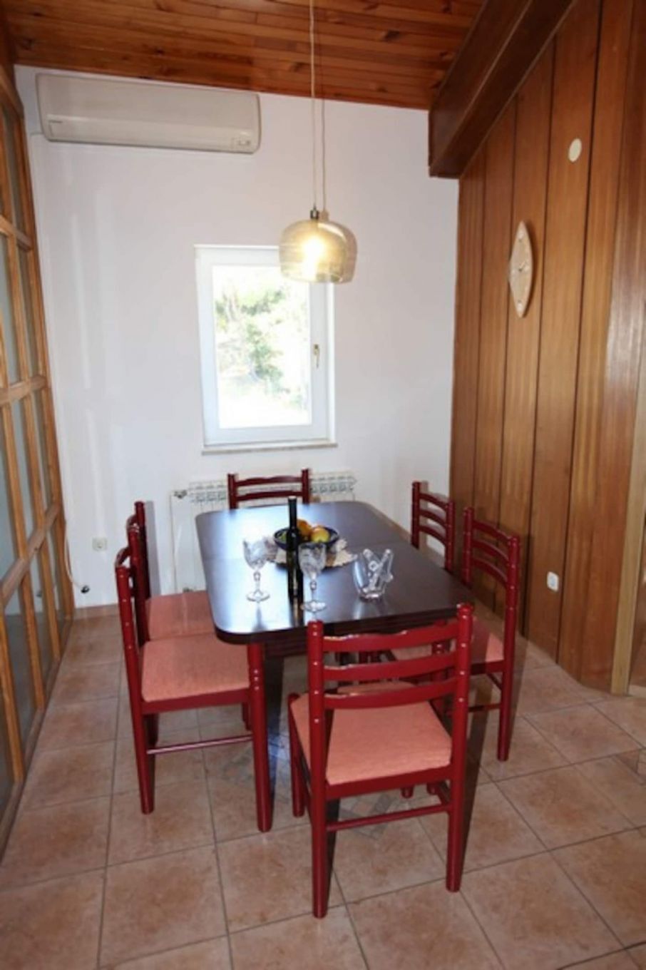 Un comedor con mesa y sillas de madera, una lámpara colgante y una ventana con vistas.
