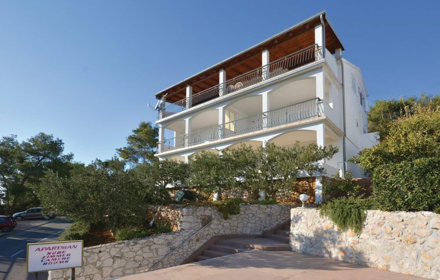 A two-story building with balconies, stone walls, and a sign indicating it is an apartment building with rooms available for rent.