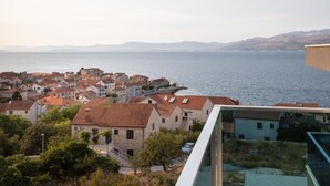 Une ville côtière aux bâtiments aux toits de tuiles rouges, offrant une vue dégagée sur la mer et surplombant une chaîne de montagnes lointaine.