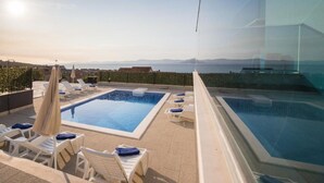 Un espace piscine sur le toit, comprenant deux piscines, des chaises longues et des parasols.