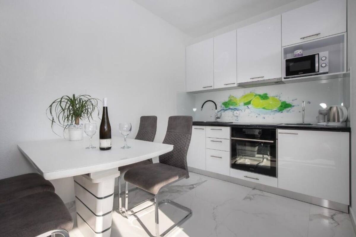 Une cuisine moderne avec des meubles blancs, un four à micro-ondes, un four traditionnel et une table à manger avec deux chaises.