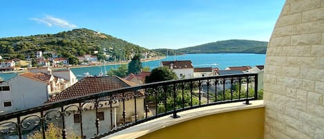 En balkong med en gul vägg och utsikt över en kuststad, med hus och en vattenyta.