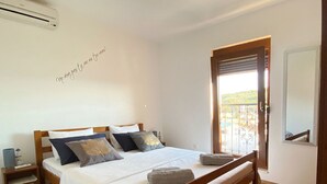A bedroom with a wooden bed, white bedding, a colorful striped rug, and a ceiling light. - House DMS (Tisno)