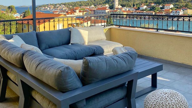 A balcony with a grey sofa set, a round ottoman, and a pergola structure. - House DMS (Tisno)