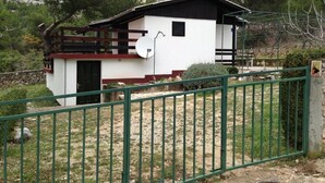 Ein zweistöckiges Haus mit weißem Anstrich und dunklen Akzenten, einer Satellitenschüssel und einem eingezäunten Garten.