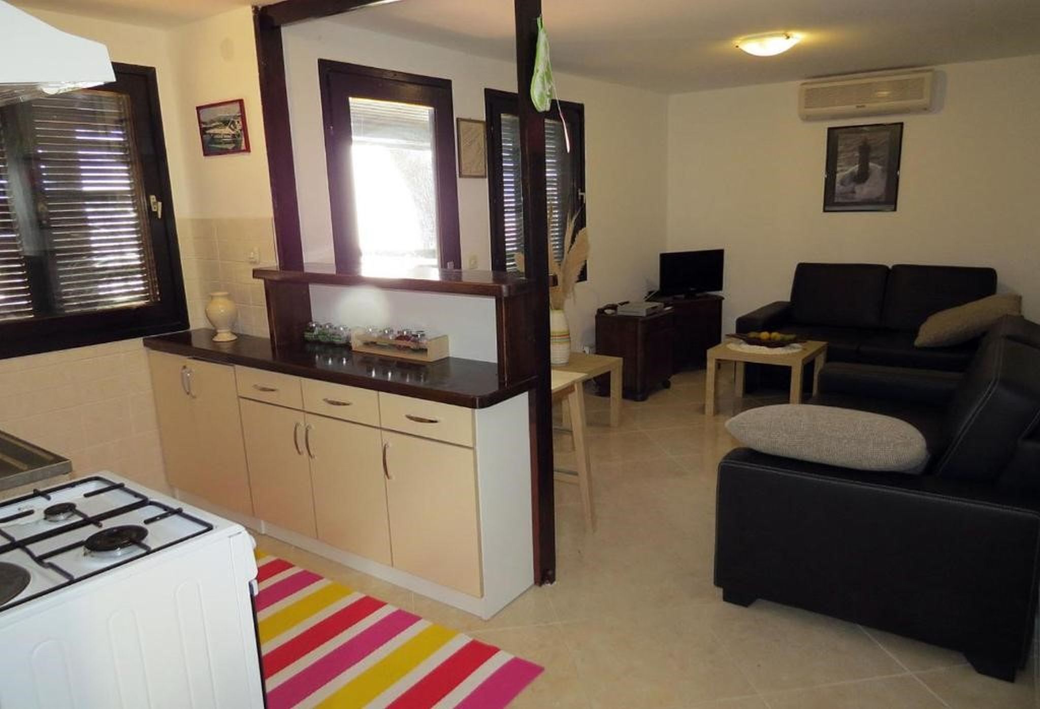 Un espacio habitable compacto con kitchenette, un sofá negro y un televisor.