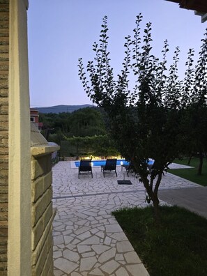 Eine Terrasse mit Steinboden, einem Pool und Liegestühlen.
