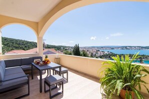 Un balcon agrémenté d’un canapé, d’une table et d’un pot de fleurs, offrant une vue sur une ville côtière et la mer.