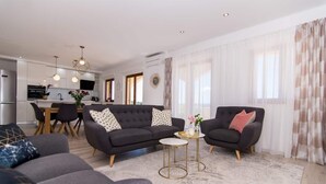 A modern living room with a sofa, two armchairs, a coffee table, and a dining area with a kitchen in the background. - Apartment Tom (Trogir)