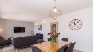 A modern living room with a wooden dining table, grey sofas, a TV mounted on the wall, and a decorative clock. - Apartment Tom (Trogir)