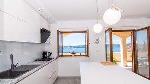 A modern kitchen with a view of the sea, a dining area, and a balcony. - Apartment Tom (Trogir)