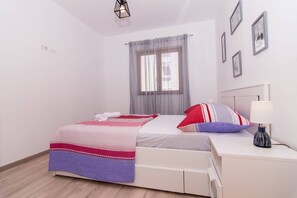 Une chambre bien rangée, avec un lit, une table de chevet, une lampe et une fenêtre avec des rideaux.