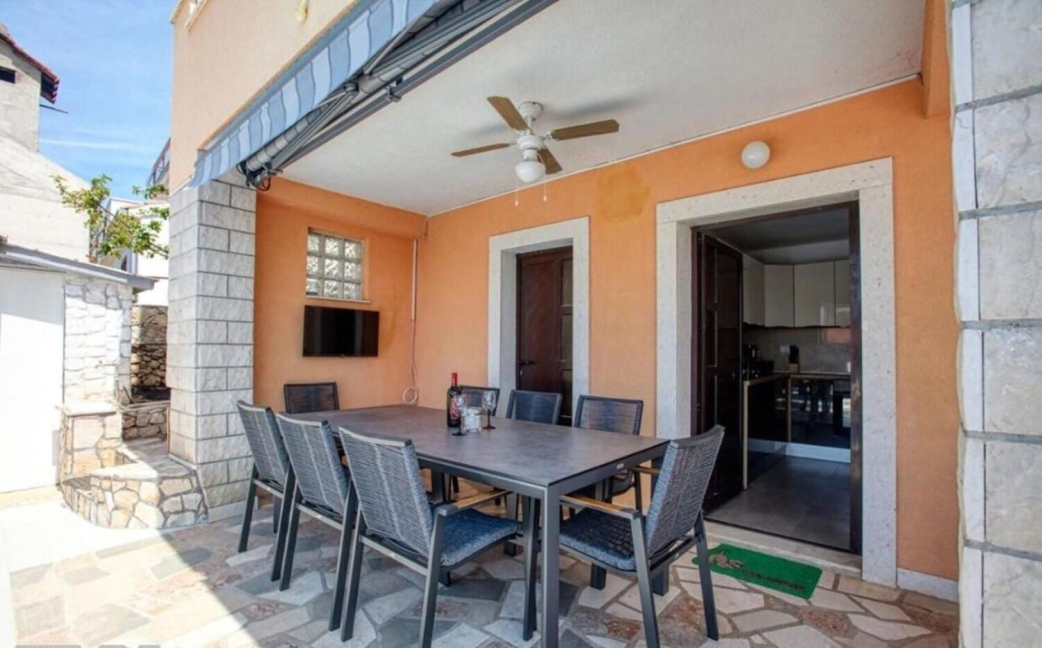 An outdoor patio with a table and chairs, a ceiling fan, and a stone wall.