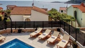 Un espace piscine doté de chaises longues, offrant une vue dégagée sur la mer, et des bâtiments coiffés de toits en tuiles rouges.